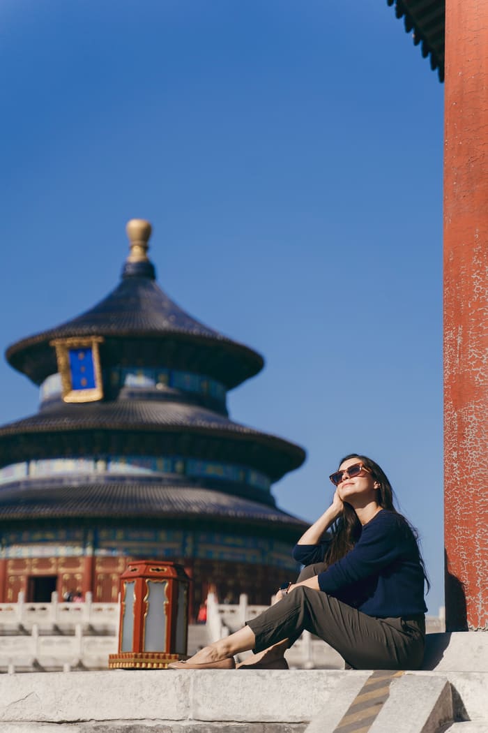 Turista sentada frente a un palacio chino, día soleado con cielo azul