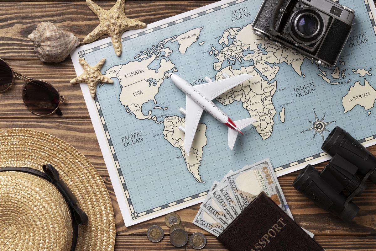 foto de un mapa sobre la mesa con un avión, una camaral, pasaportes y un sombrero