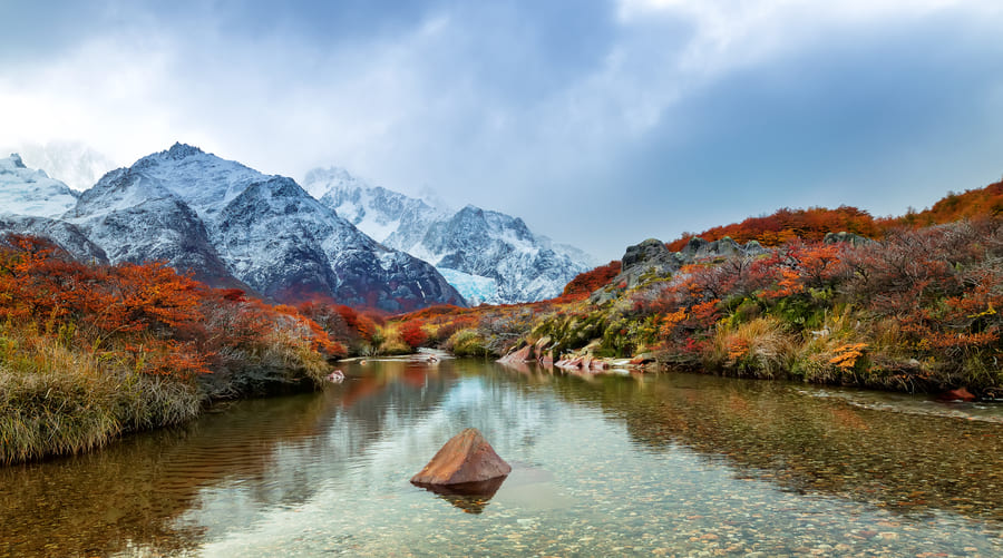 Paisaje de Yunnan, de fondo una montaña nevada y en primer plano un rio con vegetación en colores otoñales